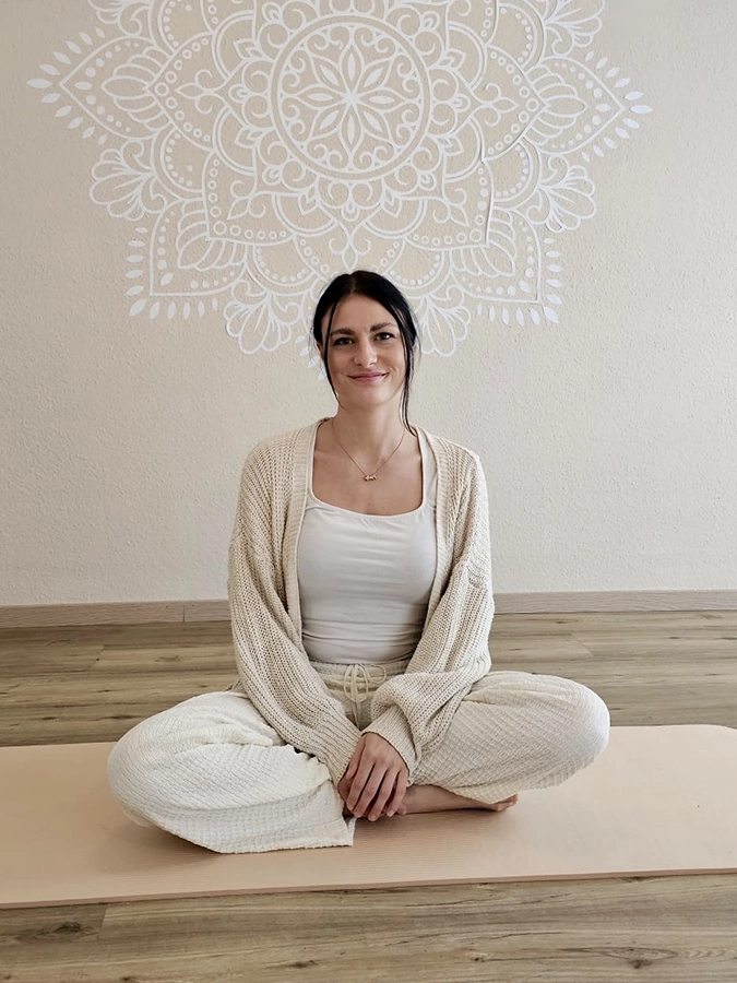 Hypnobirthing Kursleiterin sitz auf einer beigen Yoga Matte in einem hellen Studioraum